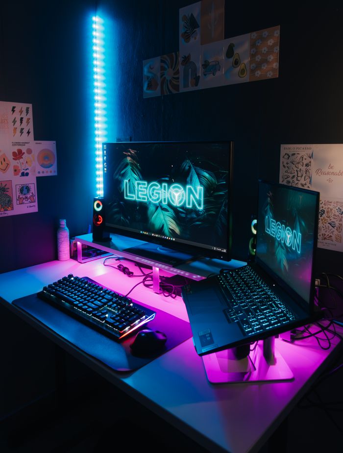 Gaming setup with neon lighting featuring dual monitors and RGB keyboards on a stylish desk.