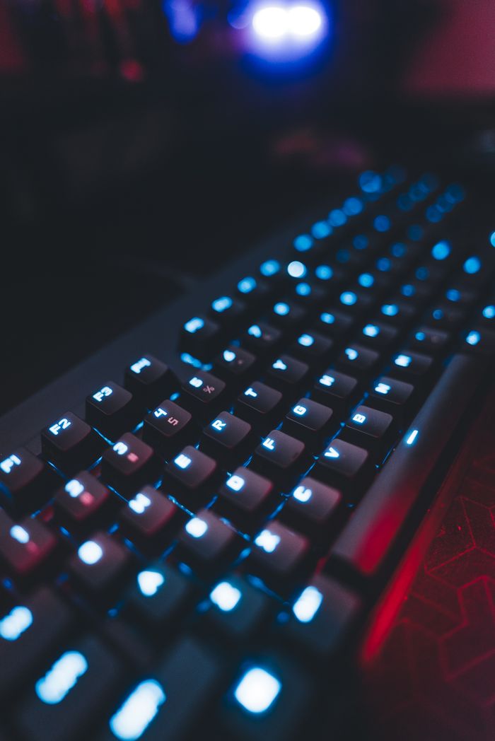 Vibrant and moody gaming keyboard with blue backlight in a dimly lit room.